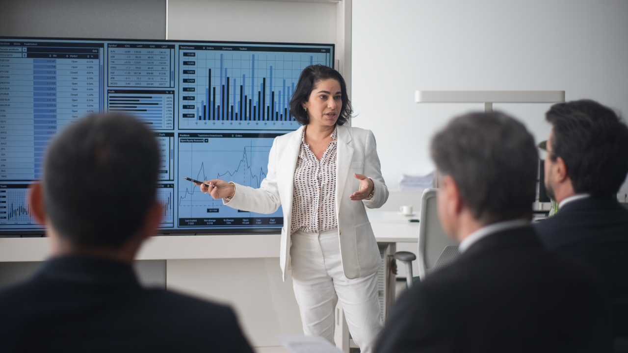 A female executive in a white suit leads a presentation on business strategy and market trends.