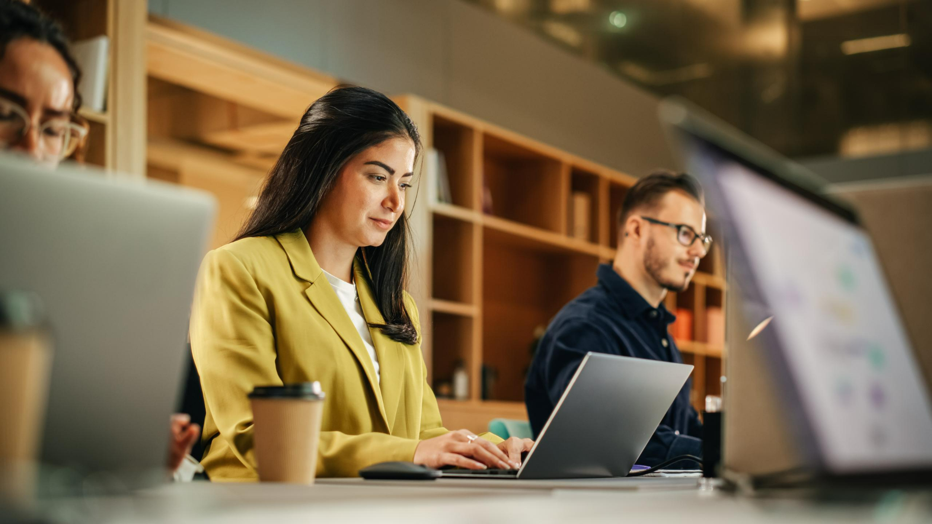 Group of Diverse Creative Team Members Using Laptops in an active Contemporary Office. Young Female Media Relations Manager Working on Brand Innovation Strategy and Collaborating with Colleague