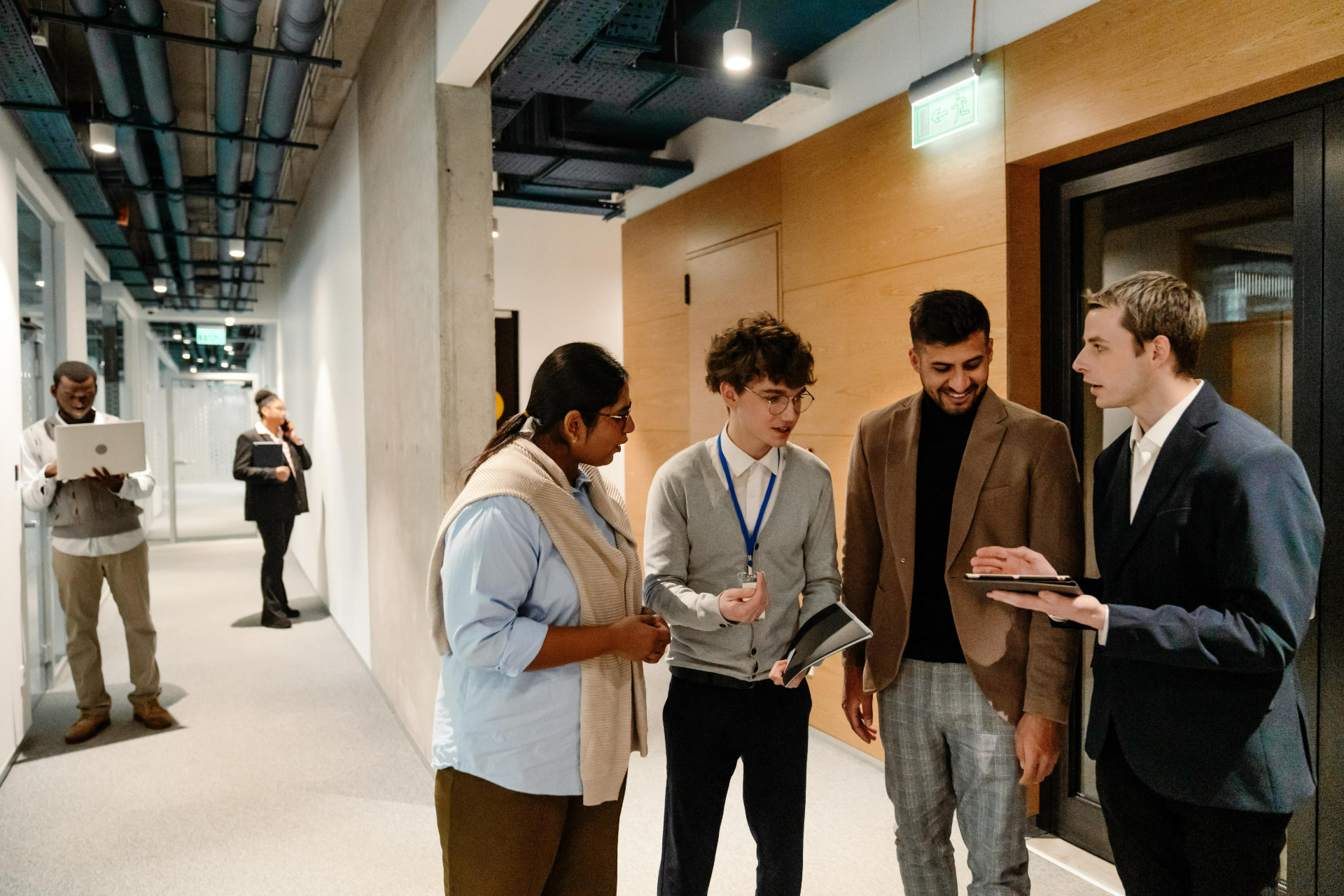 In the hallway of a modern office four young colleagues of different ethnicities are animatedly discussing work tasks