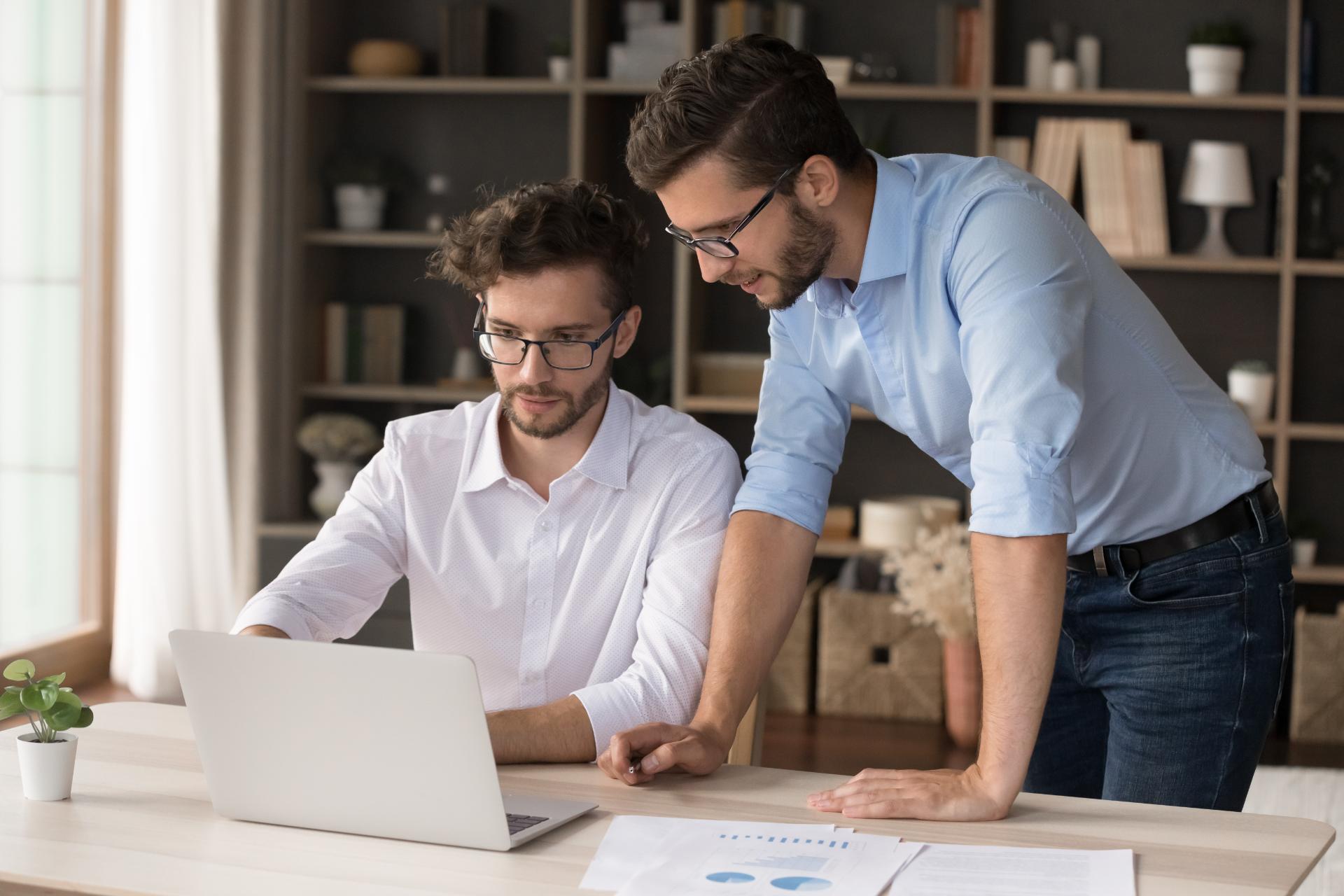 Mentoring in family business. Confident young freelance working businessman student help consult twin brother offer idea use notebook to explain financial paperwork details at home office workplace