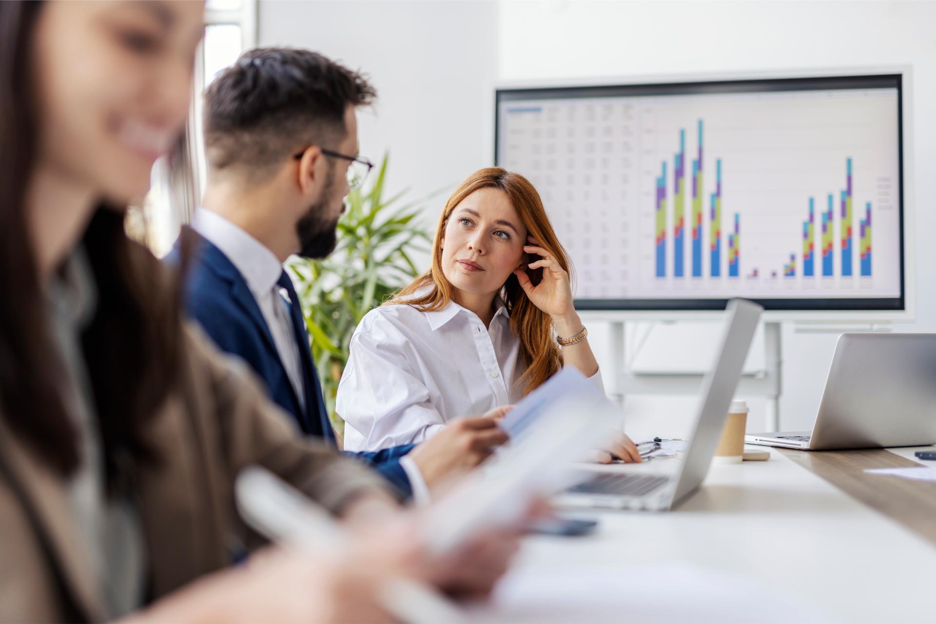 Portrait of manager sitting at conference table with her leadership team and smiling at camera during meeting