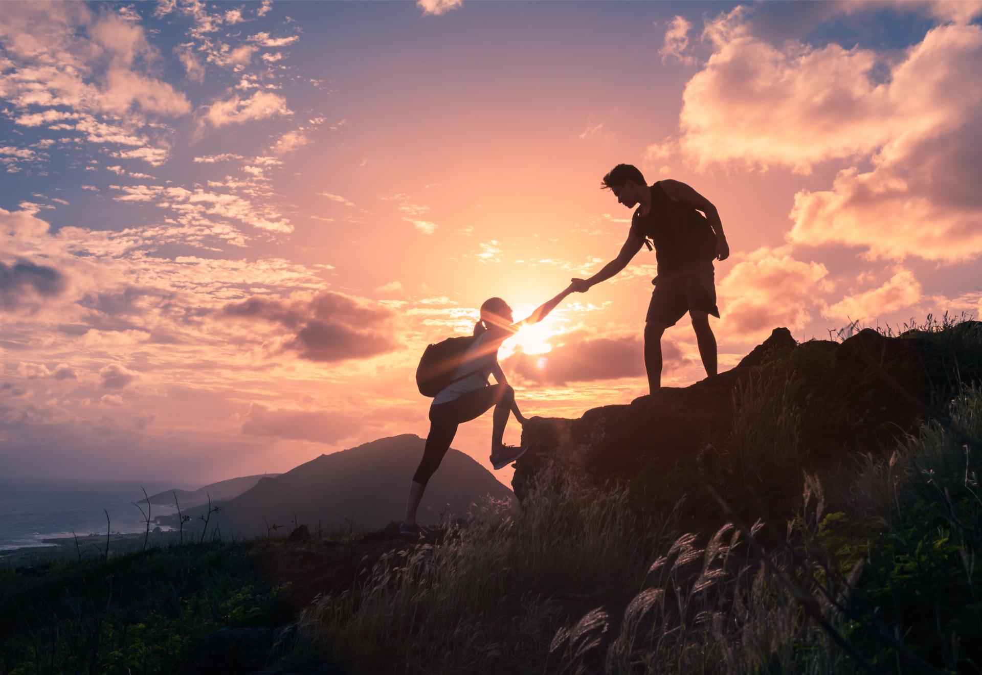 Team work life goals and self improvement concept. Man helping his female climbing partner up a steep edge of a mountain