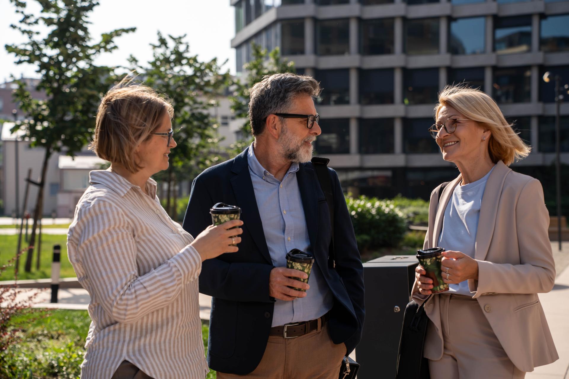 Diverse business people having coffee and water break outdoors pleasant conversation in urban business district