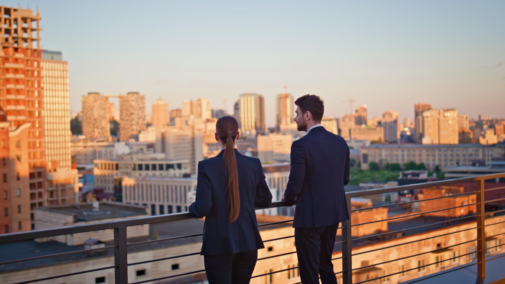 Business people standing terrace looking at cityscape in golden sunset sunlight