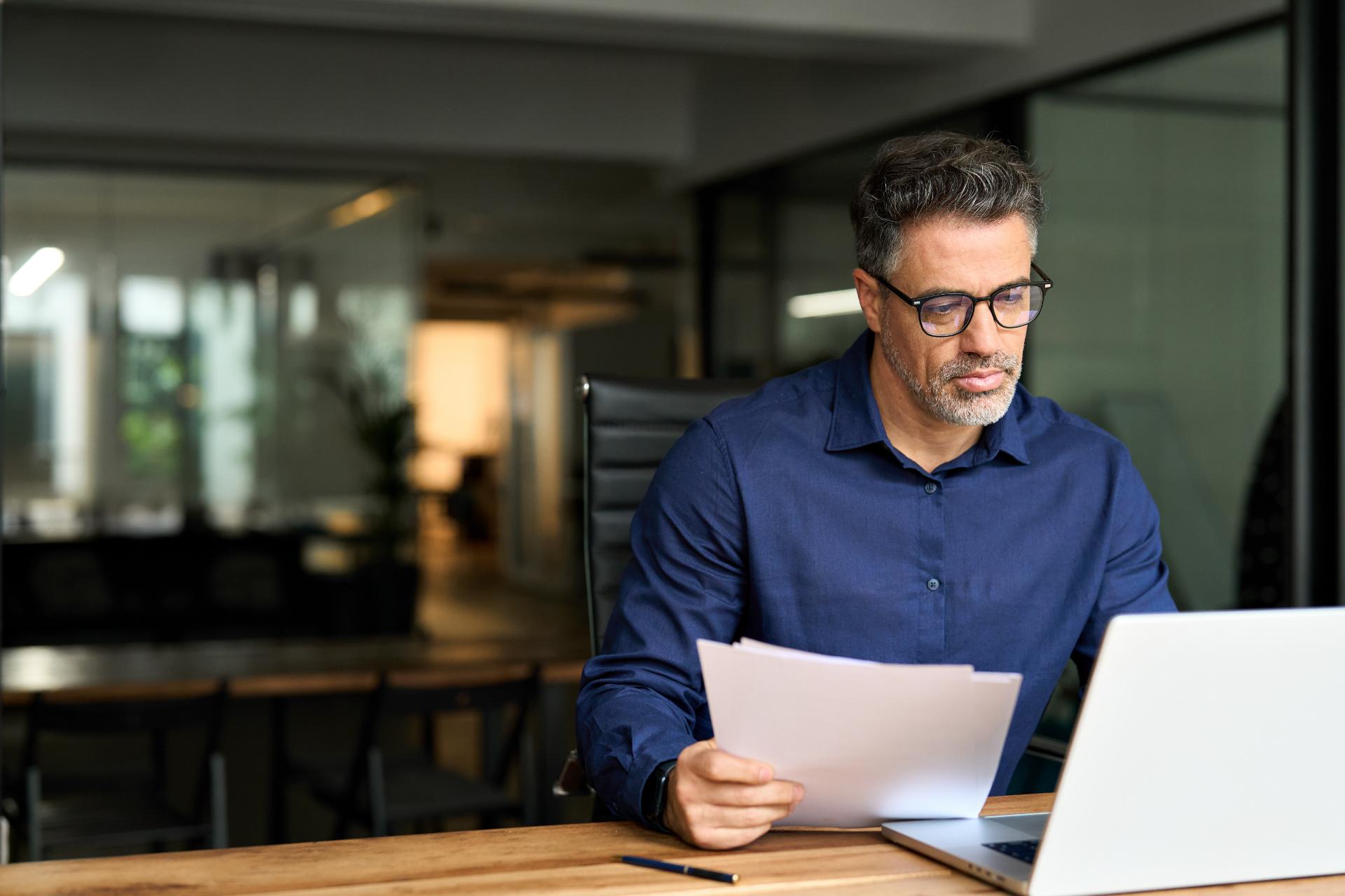 Middle aged professional business man using laptop computer reading document at work
