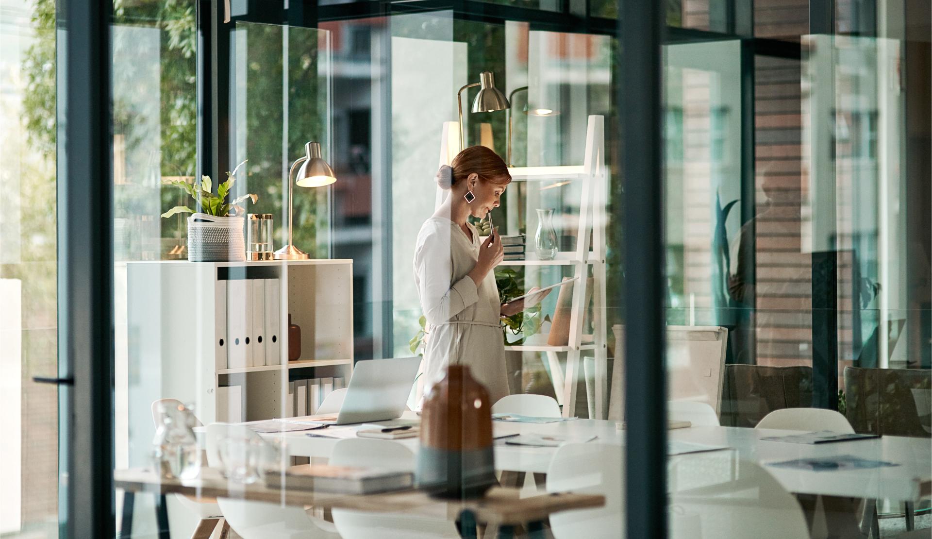 A modern office building interior and a businesswoman doing online research on a tablet or looking at files