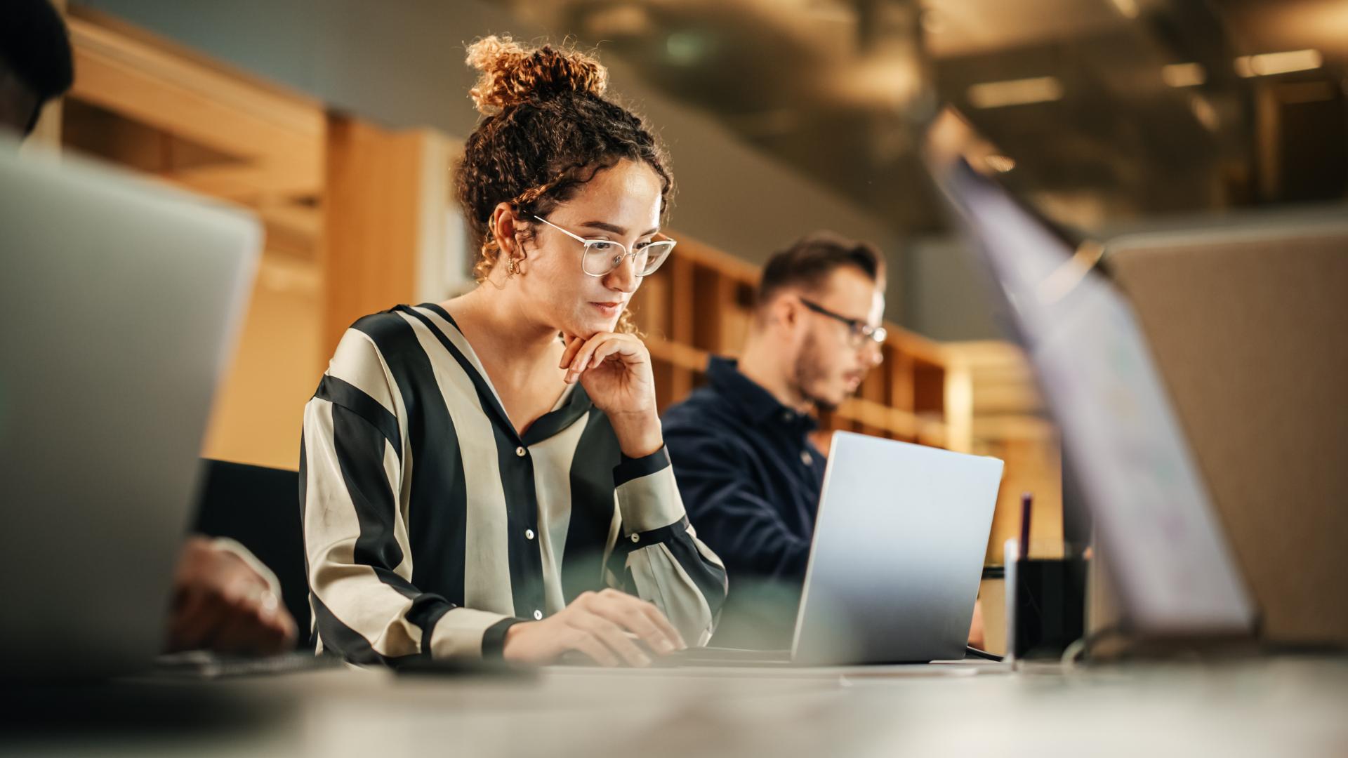 Portrait of Enthusiastic Hispanic Young Woman Working on Computer in a Modern Bright Office
